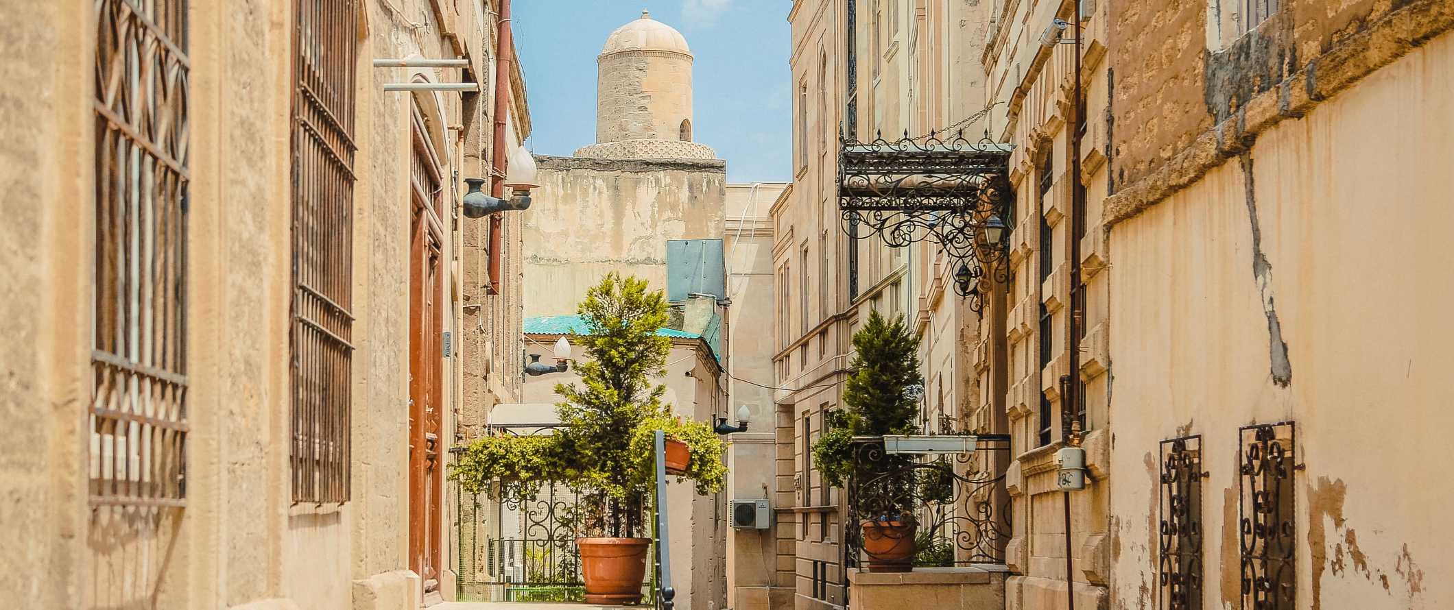Streetscape with historic beige buildings and a domed tower in the background on a bright sunny day in Baku, Azerbaijan