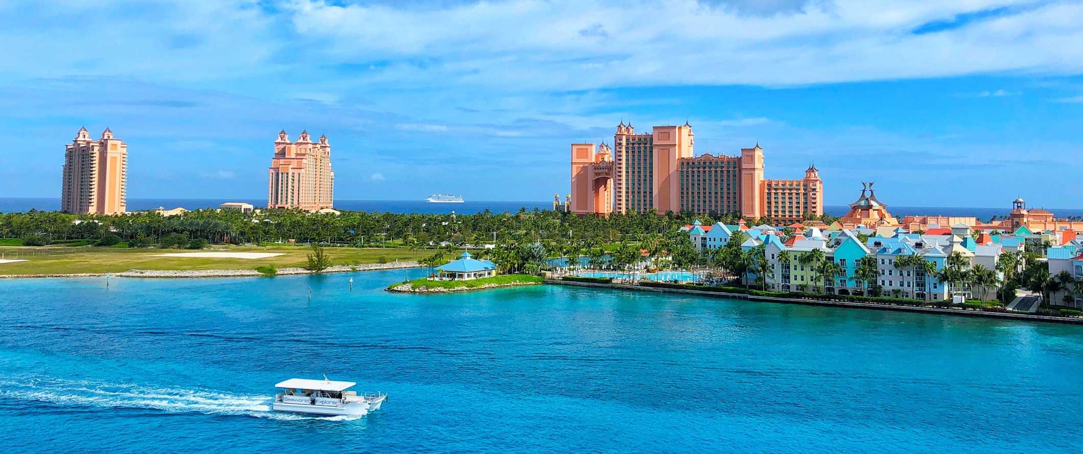 The Atlantis hotel complex in the background with a boat going by bright blue waters in theforeground, in the Bahamas
