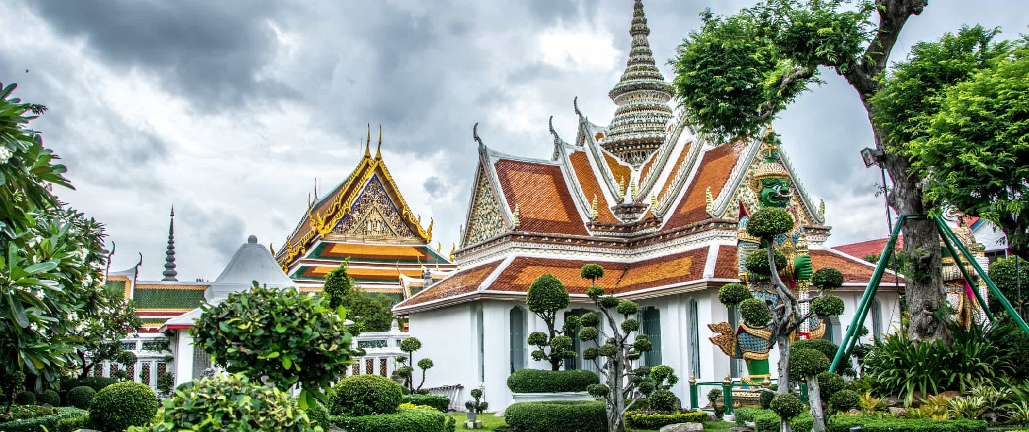 Gilded buildings in the temple complex of Wat Arun, surrounded by manicured topiary, in Bangkok, Thailand