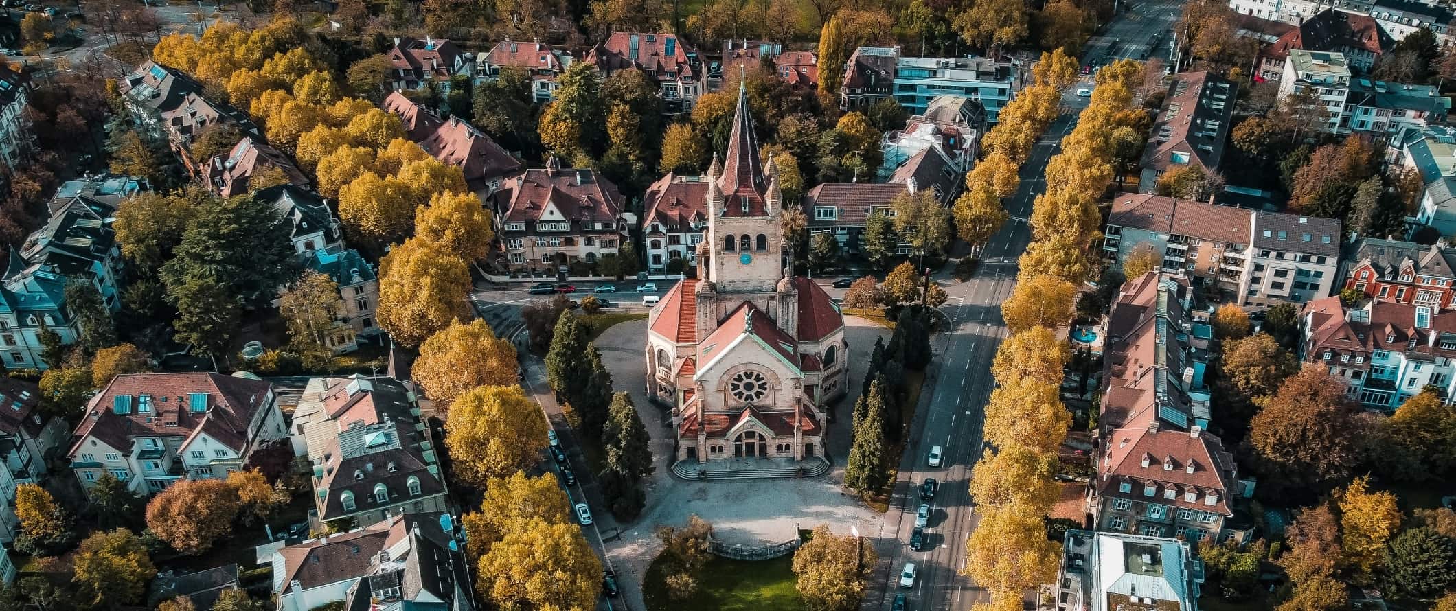 Aerial view of tree-lined streets with a historic church in a plaza in Basel, Switzerland
