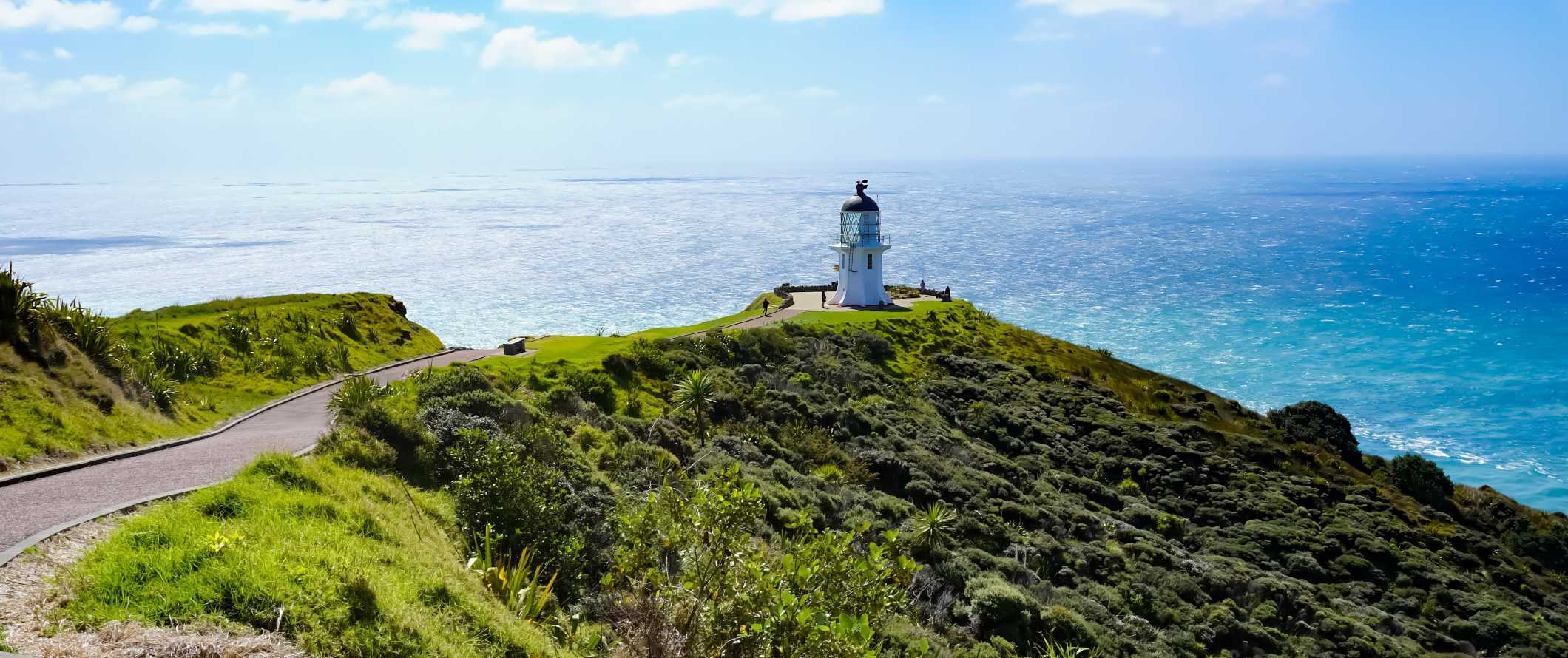 Domed white lighthouse on the edge of a lush, green cliff with the sea in the background in the Bay of Islands, New Zealand