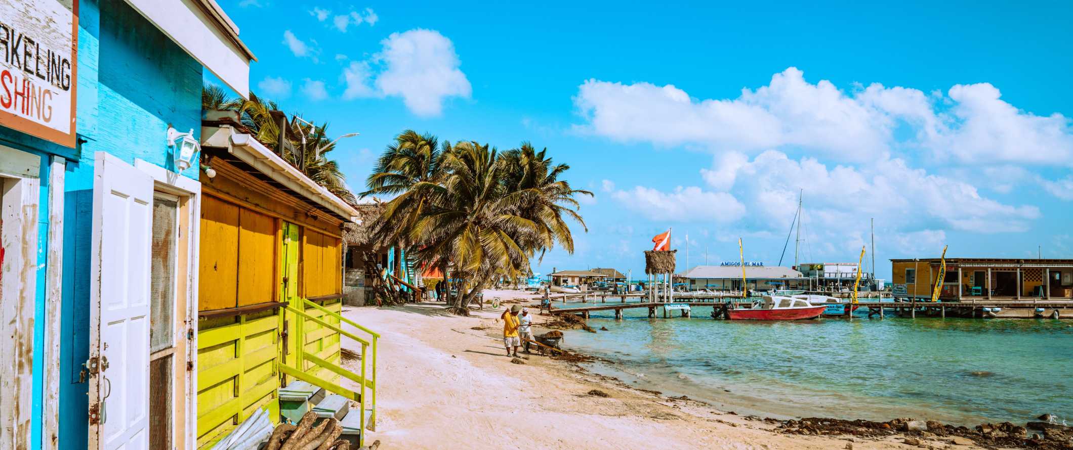 Brightly colored buildings along the beach, lined tropical palm trees in Belize