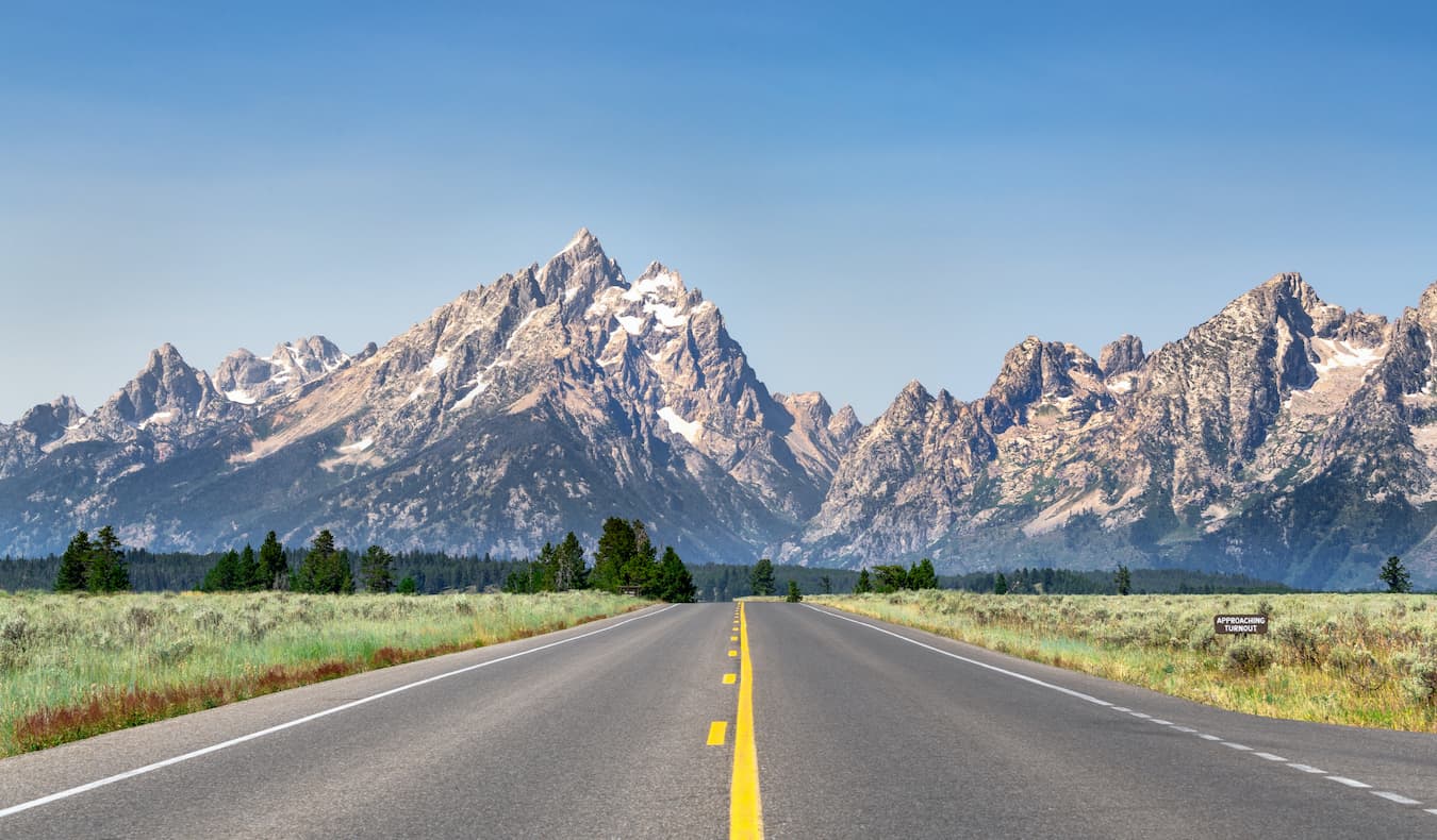 An open road on a sunny day in Wyoming, USA, with mountains in the background