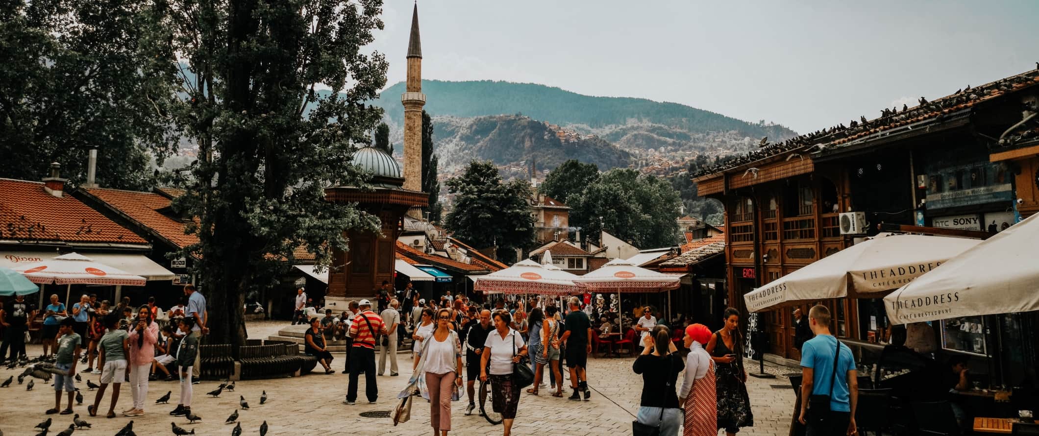 Historic square filled with pigeons and people and a minaret in the background in Sarajevo, Bosnia & Herzegovina