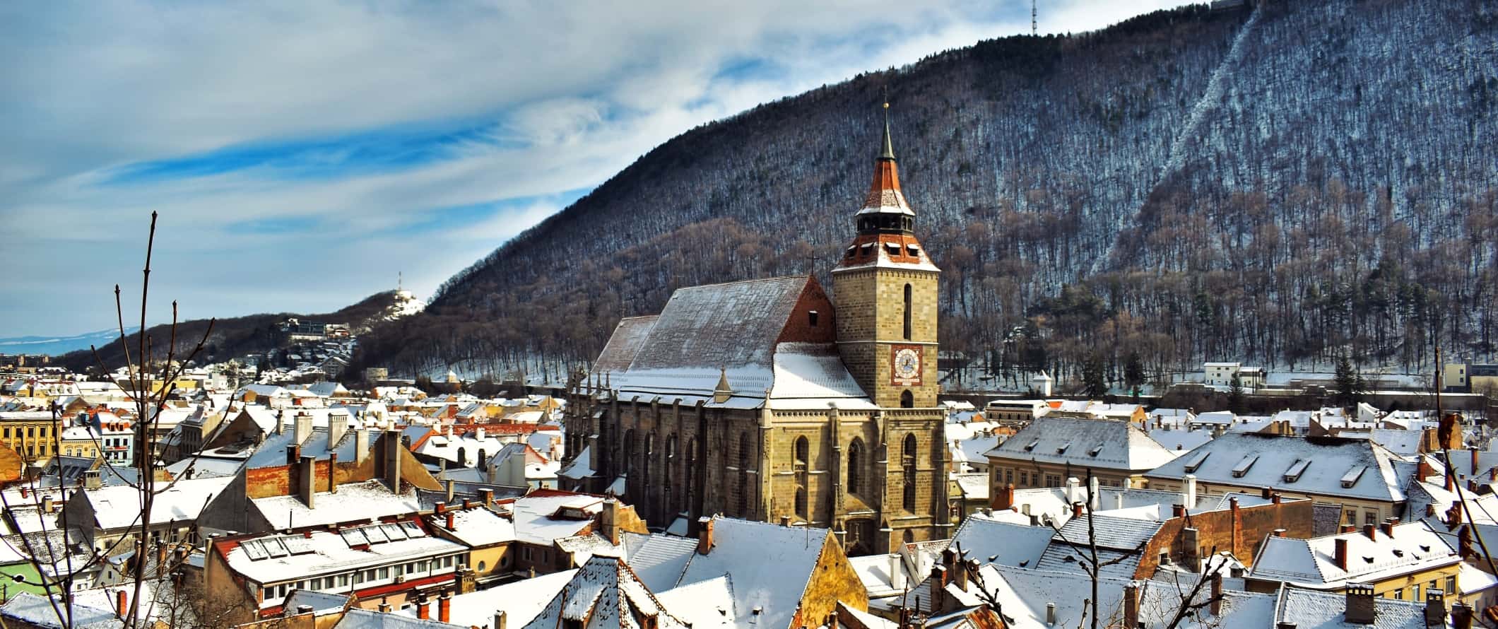 The 14th-century Black Church towering over snow-capped buildings in Brasov, Romania.
