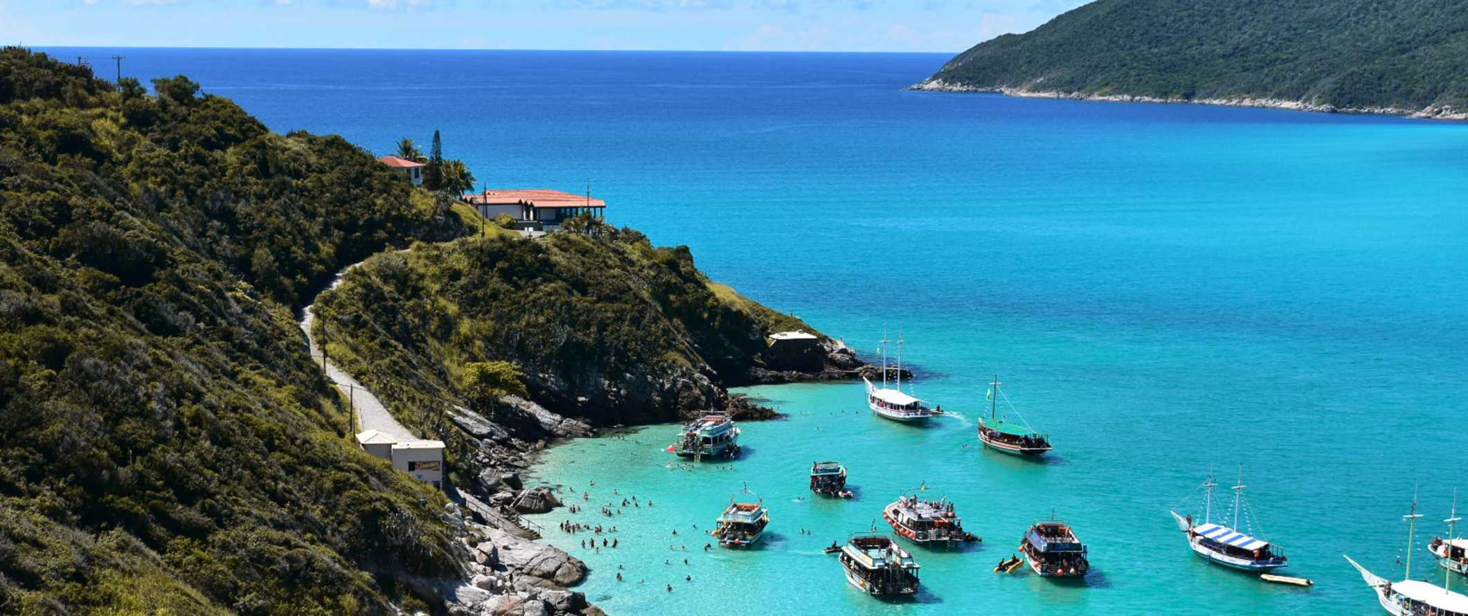 Small boats docked in clear turqoise waters along a lush green shoreline in Brazil