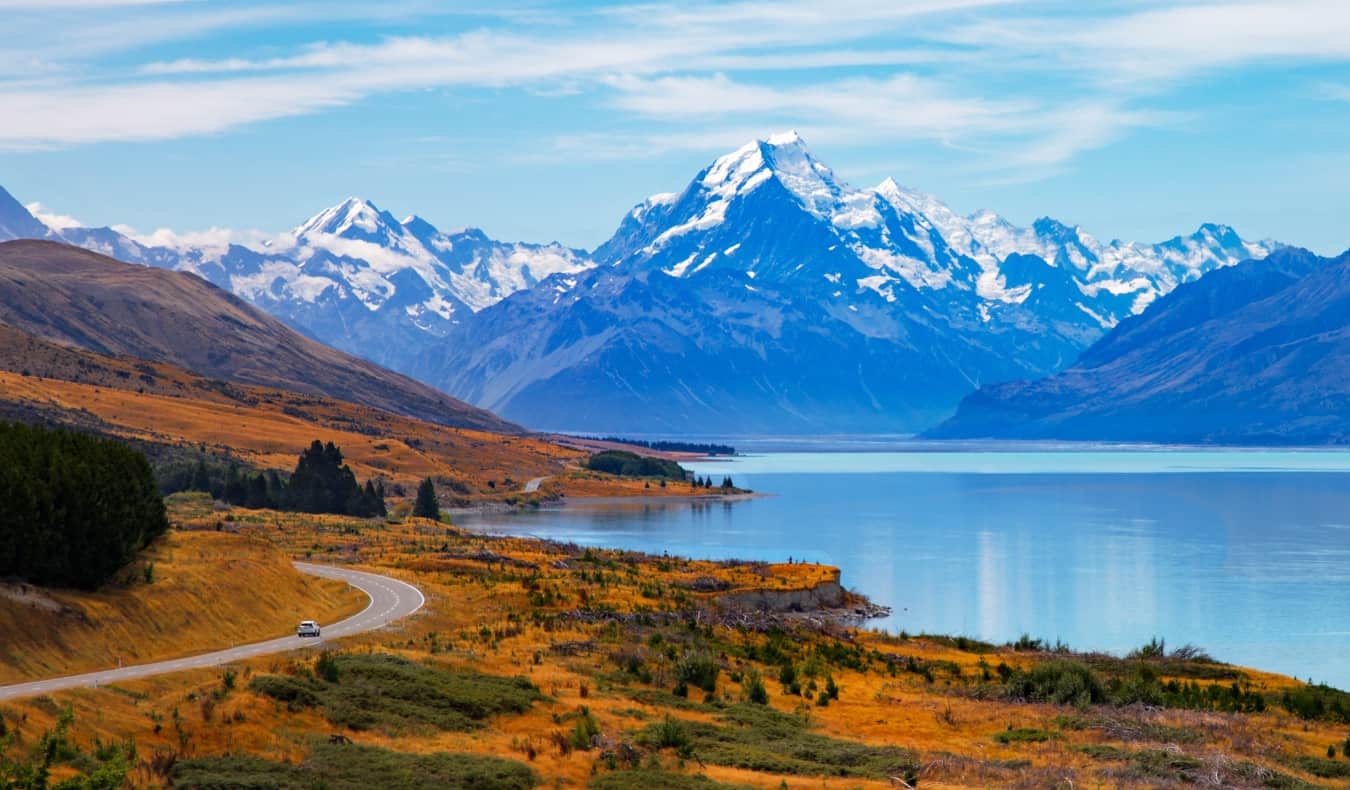 Van driving down winding road with lake and mountains in the background in New Zealand.