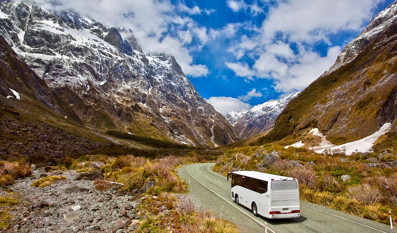 A coach bus driving through the winding roads of New Zealand surrounded by snowy mountains