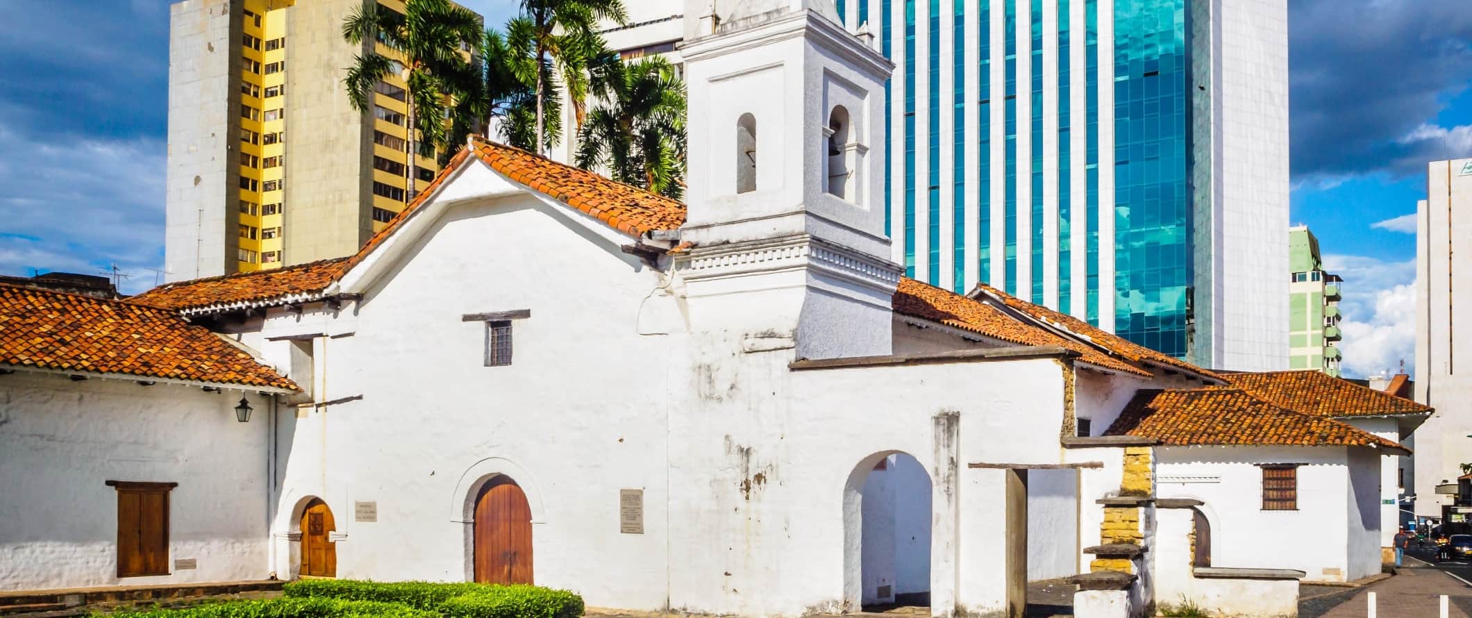 The Museum of Religious Art La Merced, a white-washed 17th-century building with a red terracotta roof set against modern skyscrapers in Cali, Colombia