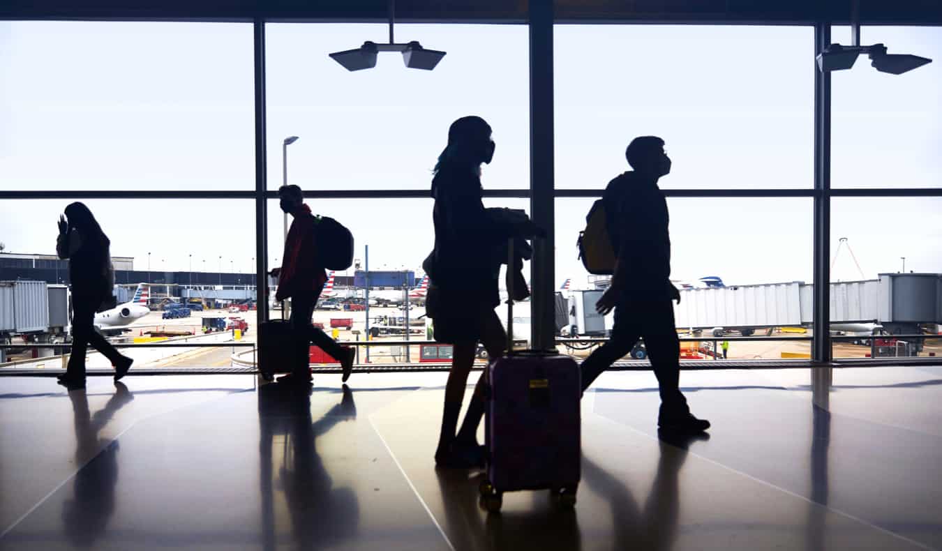 people silhouetted by a window at an airport as they walk to their gate
