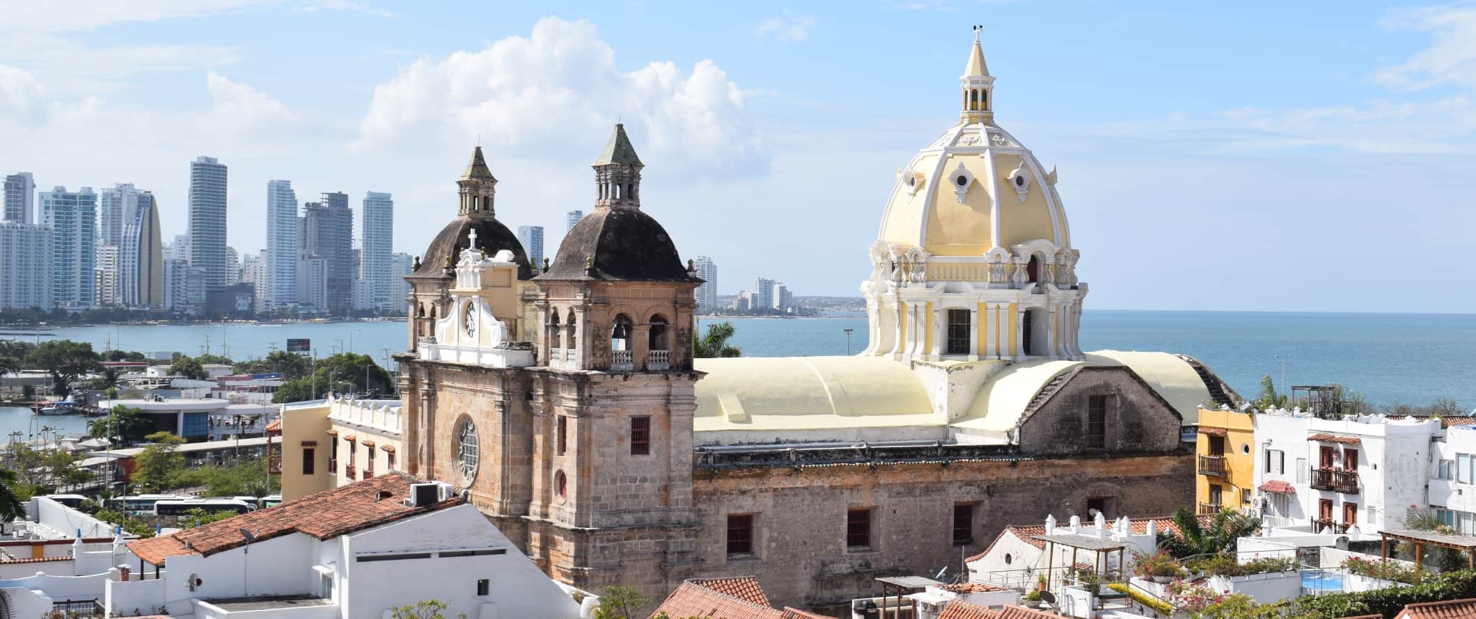 View over the walled city of Cartagena, Colombia, with a large historic domed church in the foreground and modern skyscrapers in the background