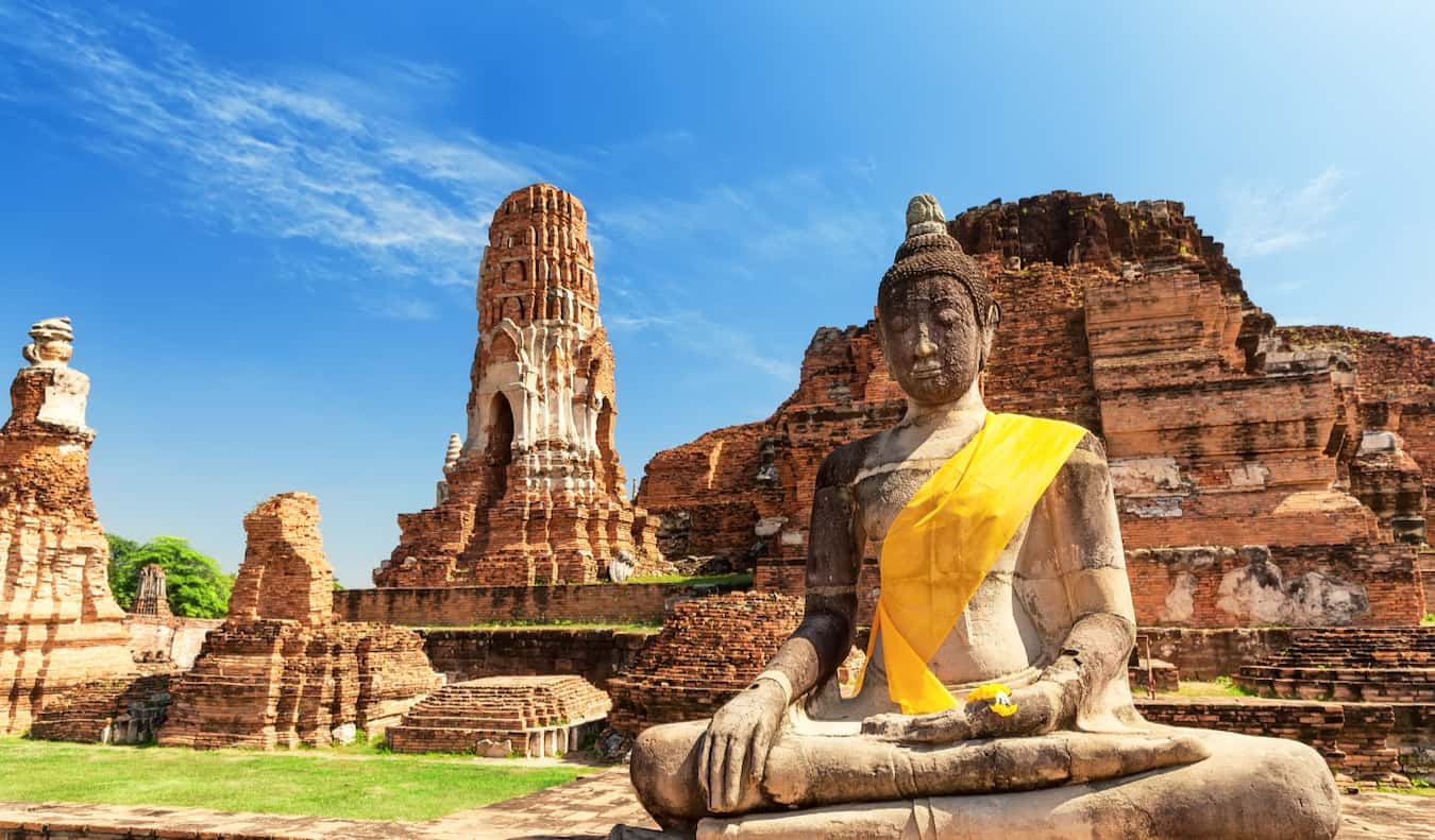 An ancient Buddha statue with a sash at a historic site in sunny Thailand
