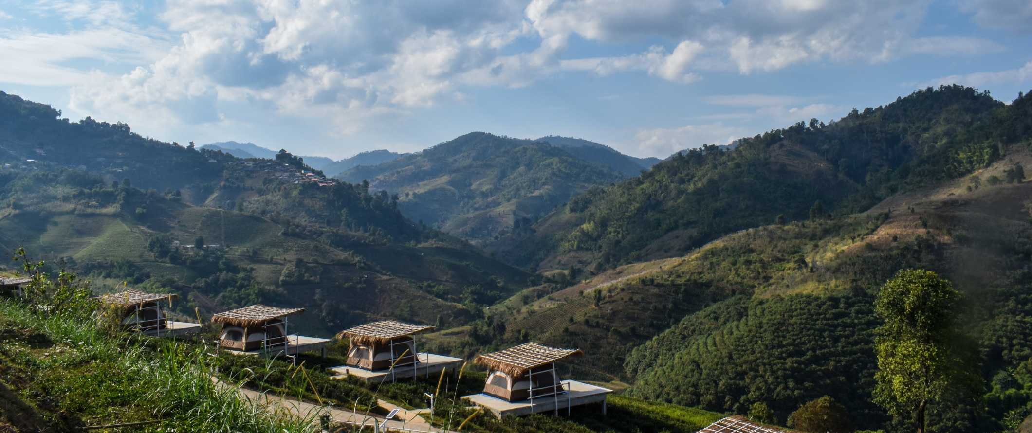 Tents on platforms in the foreground with green rolling hills in the background in Northern Thailand