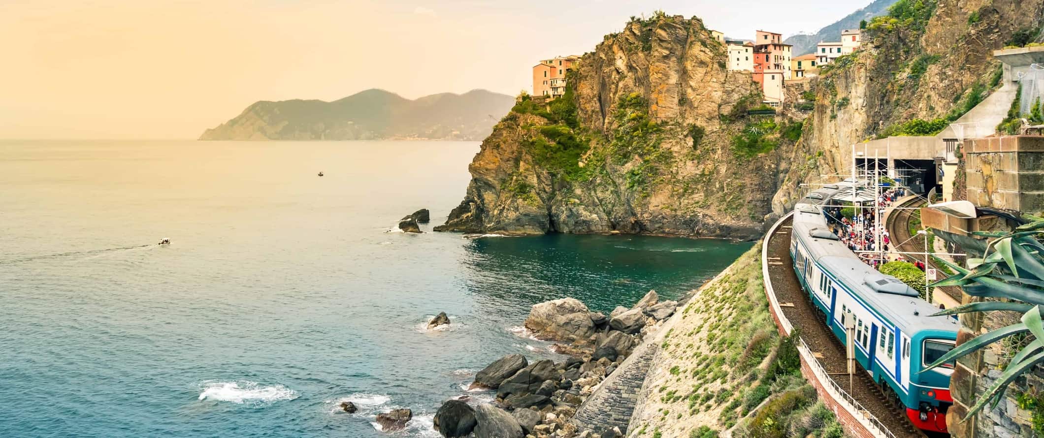 Train running along the Mediterranean seaside with rocky cliffs and villages in the background in the Cinque Terre, Italy.