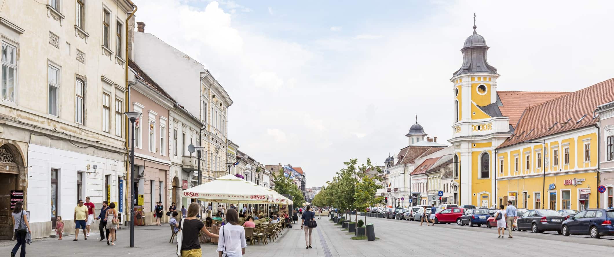 Pedestrian street with restaurant terraces and pastel-colored buildings in the city of Cluj-Napoca, Romania