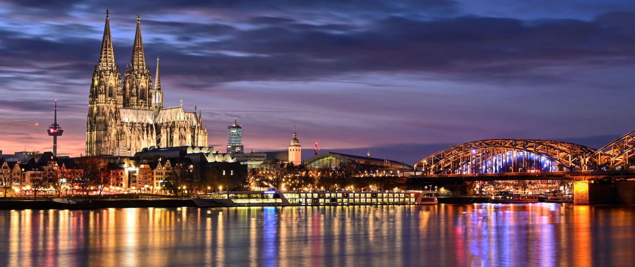 A view of the iconic cathedral and bridge lit up at night in Cologne, Germany