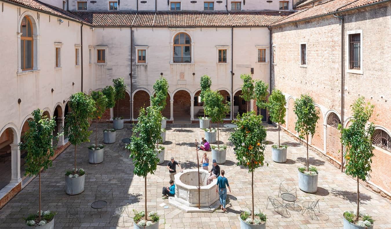 Manastir historik i mbushur me pemë portokalli dhe njerëz që qëndrojnë përreth duke biseduar në Combo Venezia, një bujtinë në Venecia, Itali.