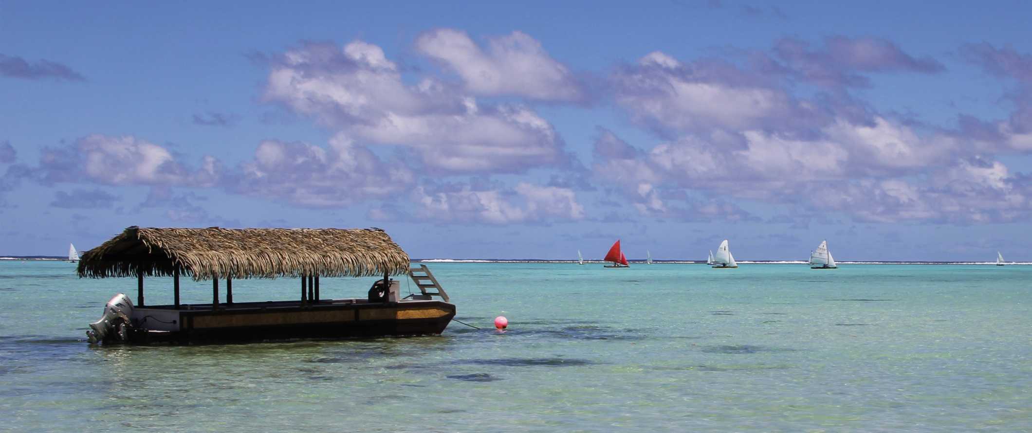 Boat with a thatched roof parked in the clear waters of the Cook Islands