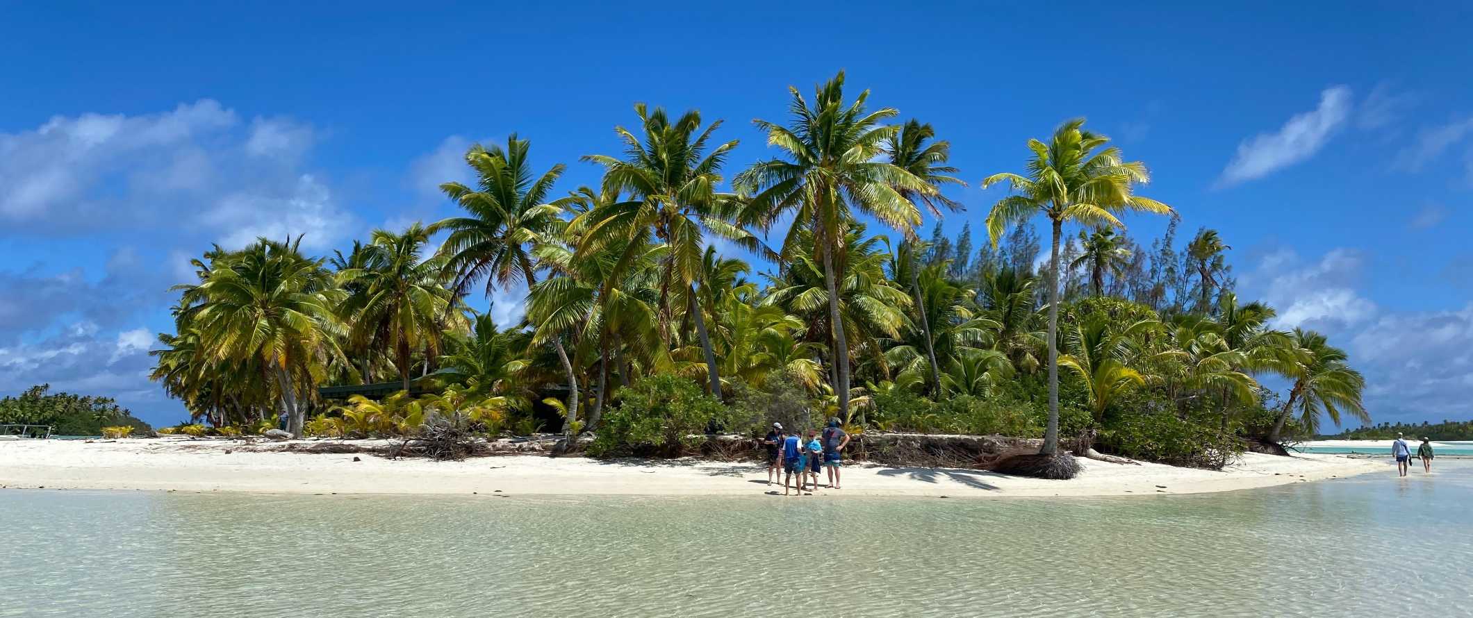 People standing on a white sand beach on the island of Aitutaki in the Cook Islands