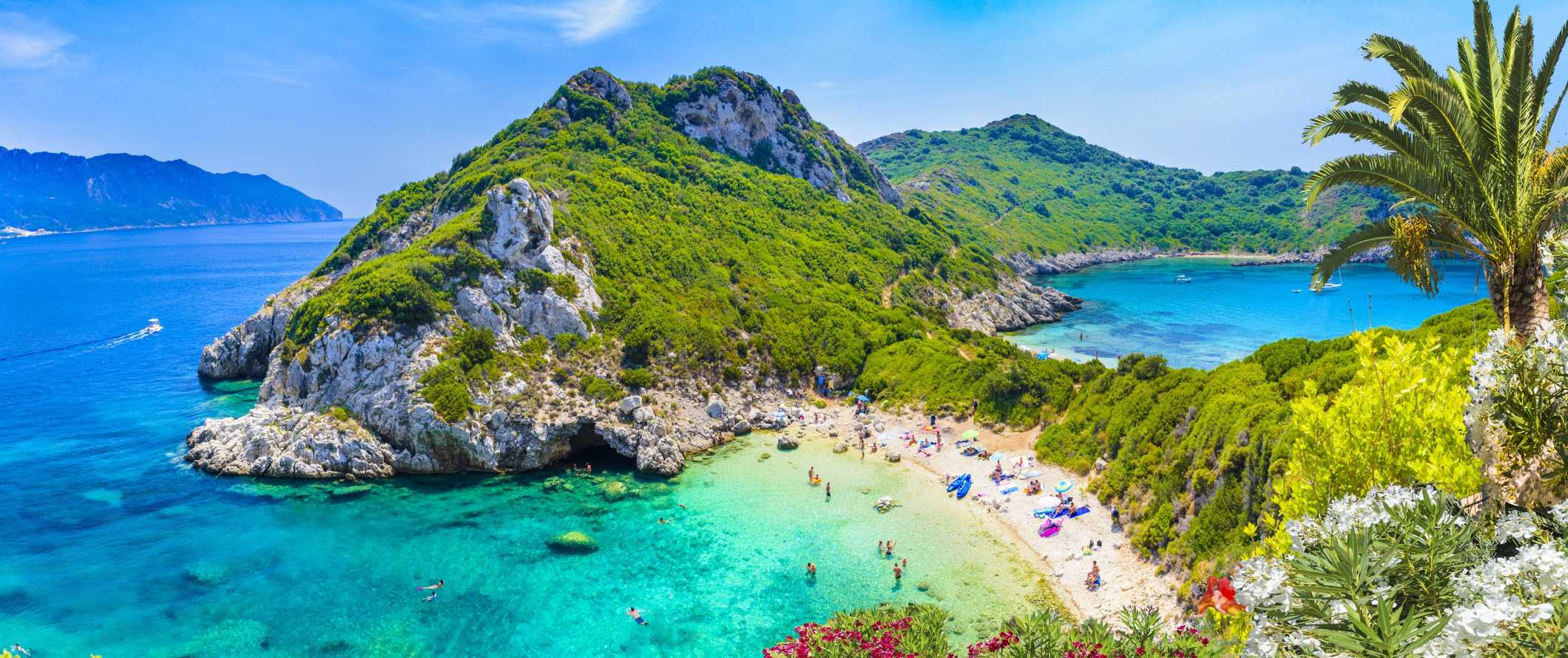 People lounging and swimming at a beach with lush hills in the background and clear, turquoise waters in Corfu, Greece