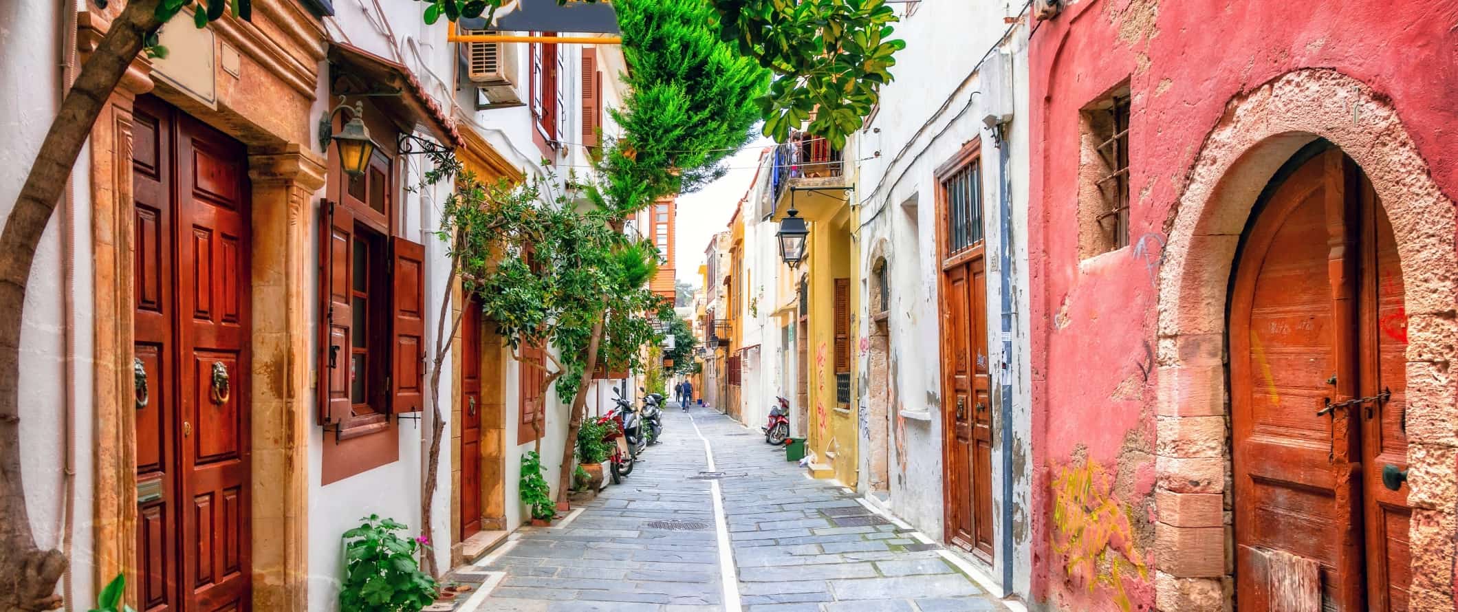 Flagstone-lined steet flanked by brightly colored houses with wooden doorways on the island of Crete in Greece.