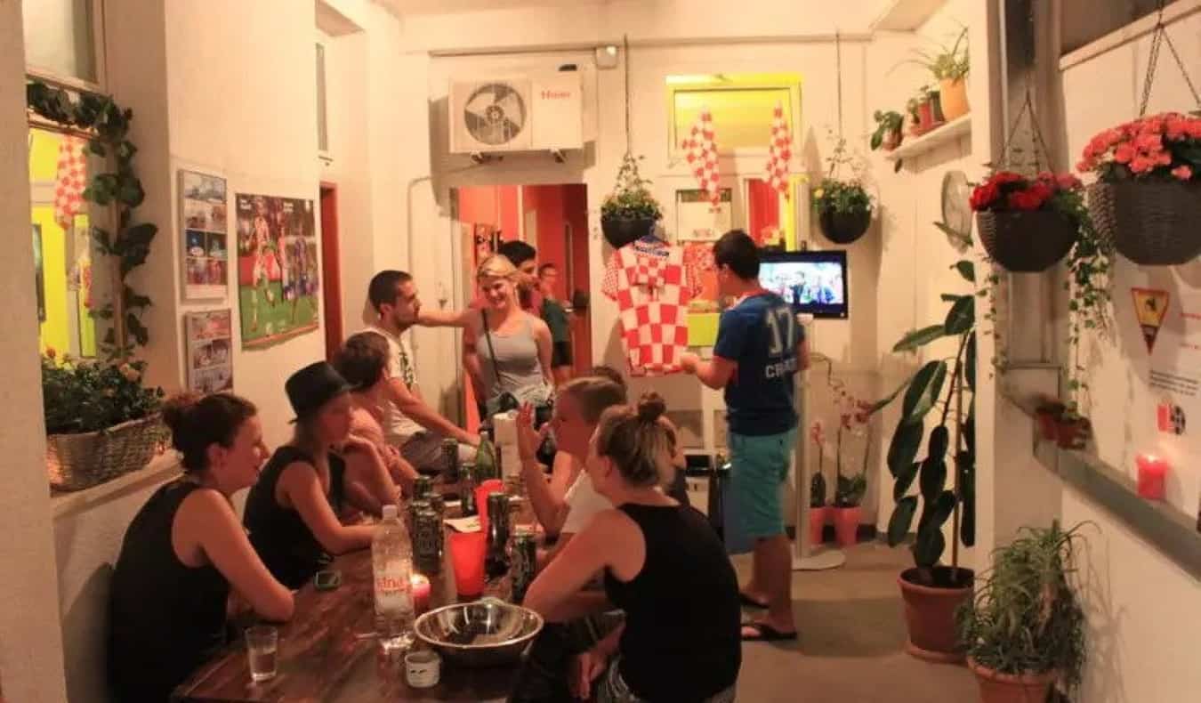 Group of backpackers sitting around a table in the plant-filled common area of Dubrovnik Backpackers Club, a hostel in Dubrovnik, Croatia.