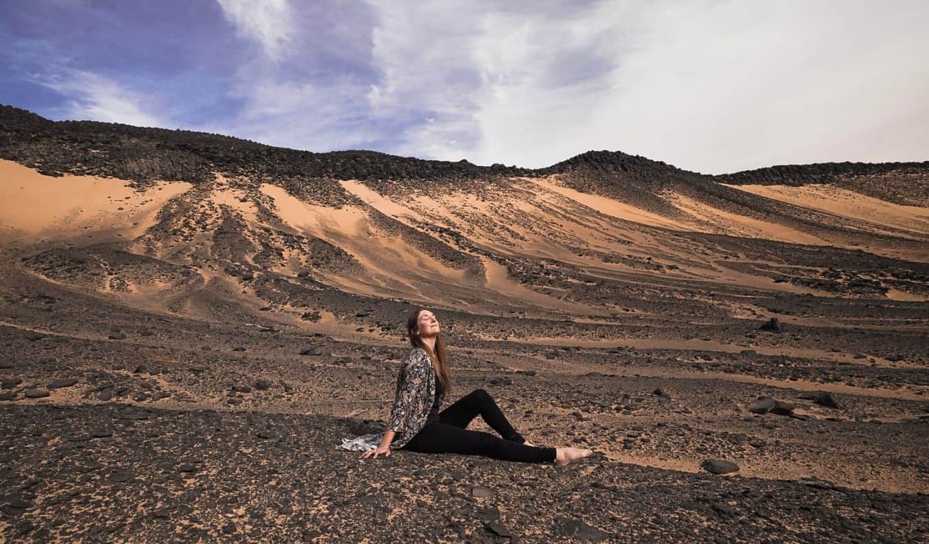 Monica, a solo traveler, sits in the desert of Egypt and poses for a photo