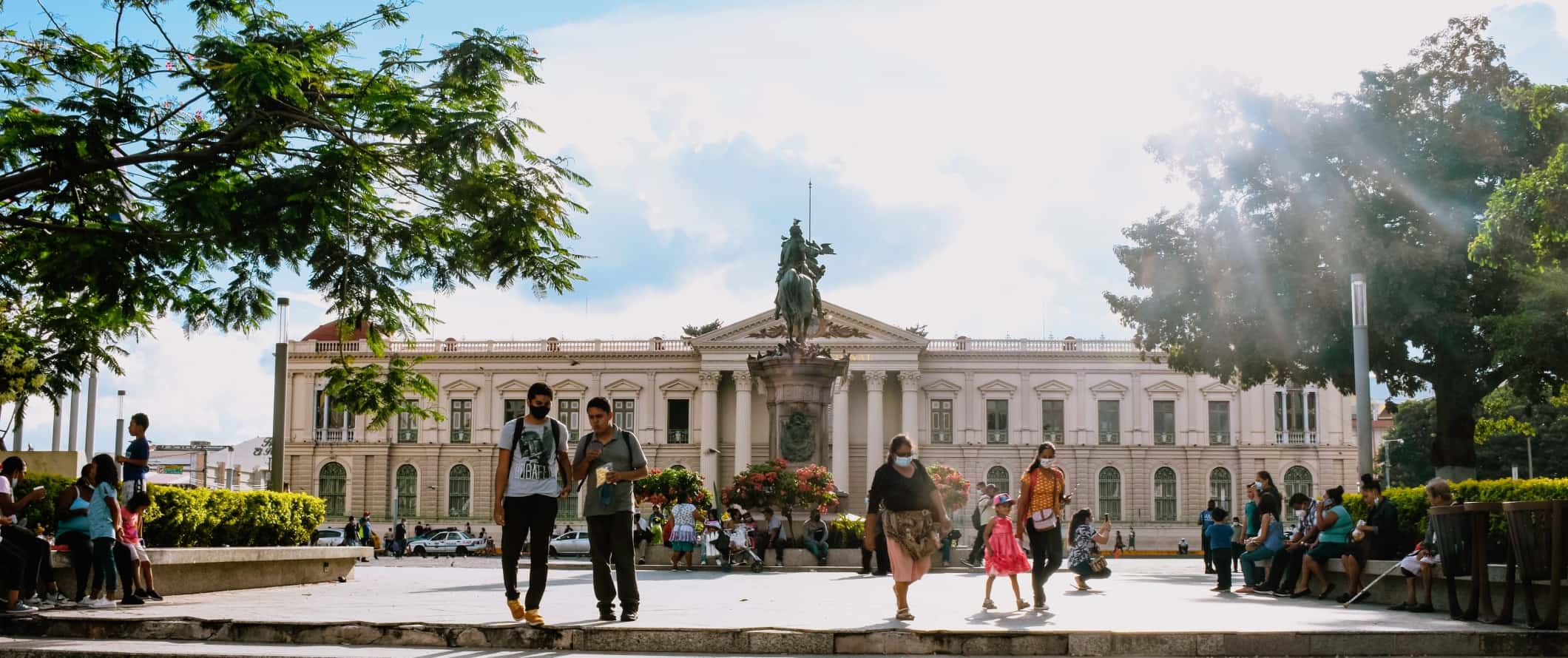 People walking around in a plaza with a historic building in the background in San Salvador, the capital of El Salvador