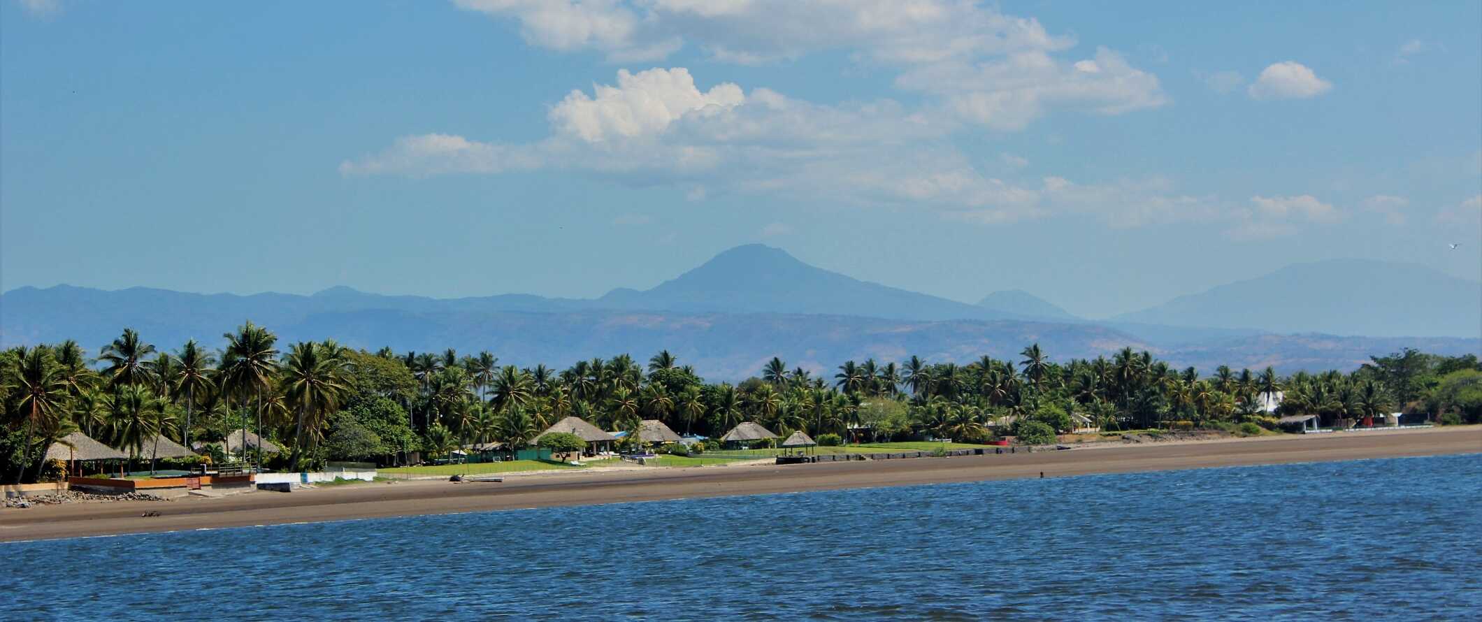 View of huts along the beach with a volcano in the background in El Salvador