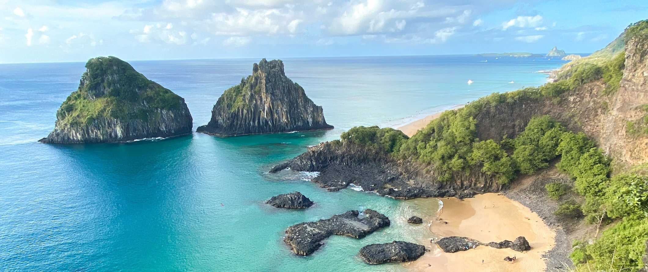 Panoramic view of beach and two large rock formations rising out of the turquoise waters of Fernando de Noronha, Brazil