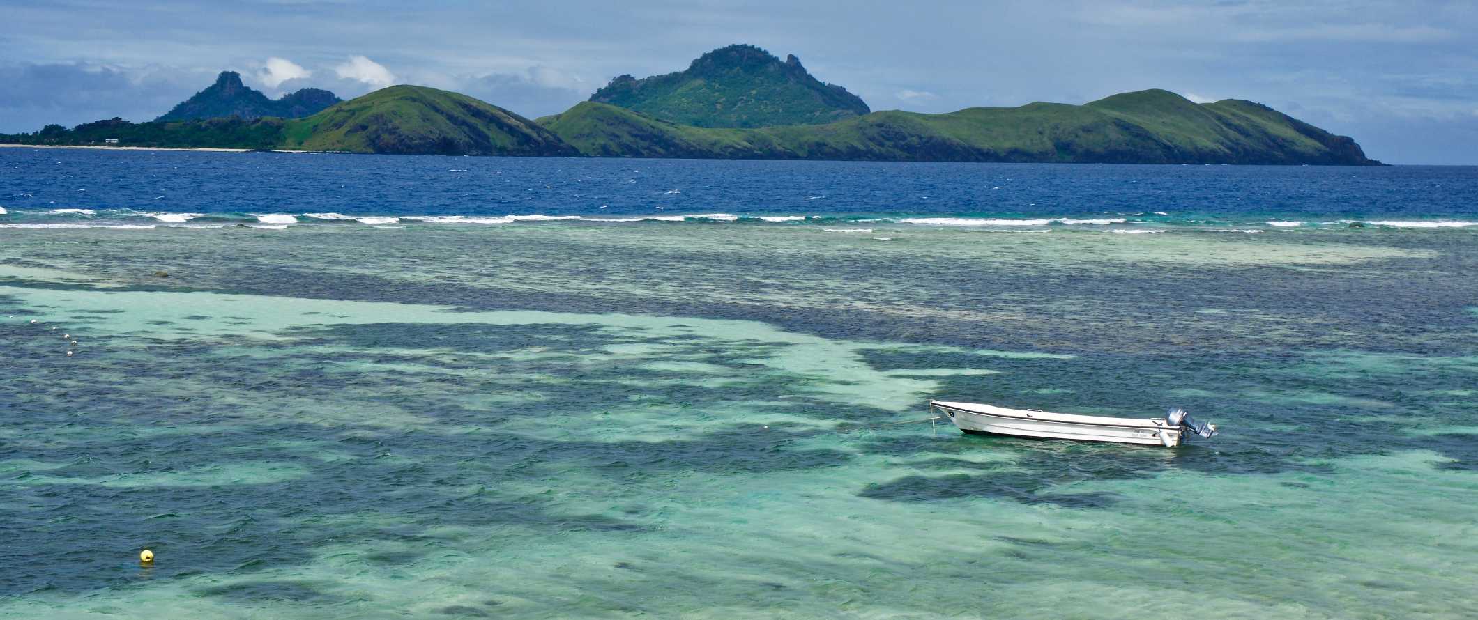 A small boat anchored in the tropical waters off the coast of an island in Fiji