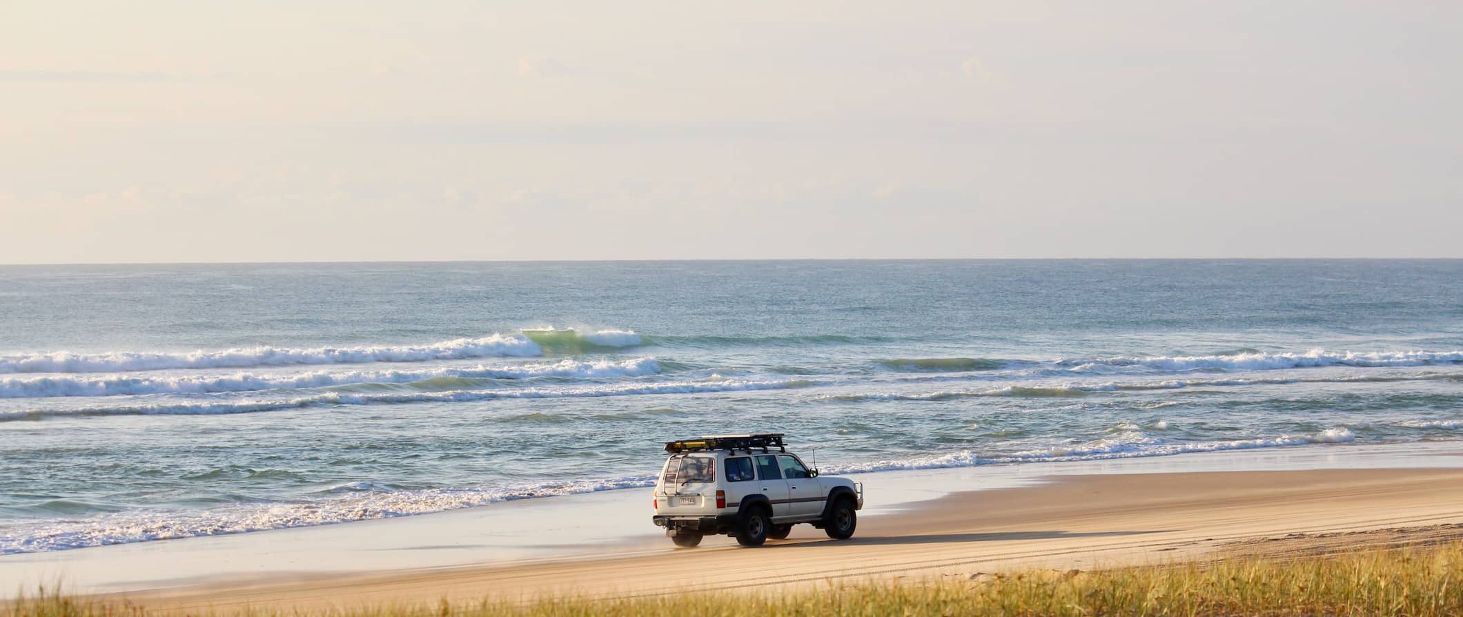 A single 4WD vehicle crusing down the wide, sandy beach of Fraser Island, Australia