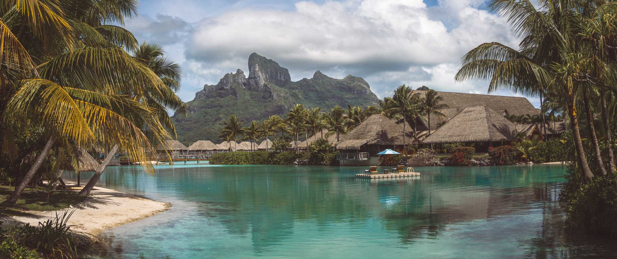 Overwater bungalows and clear waters with a sharp mountain peak rising in the background in Bora Bora, French Polynesia