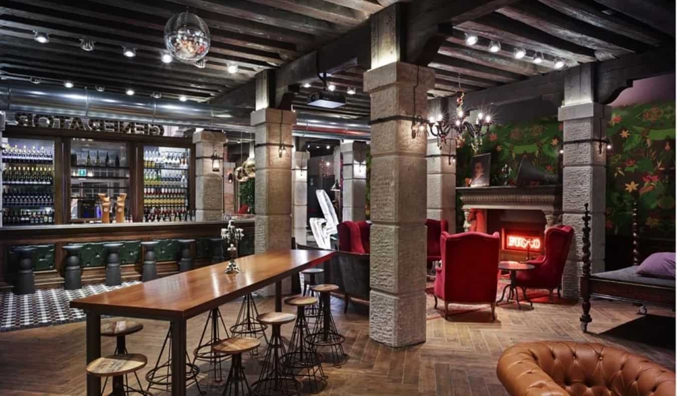 Common area with a bar, bar tables, and red comfy chairs by a fireplace at Generator hostel in Venice, Italy.