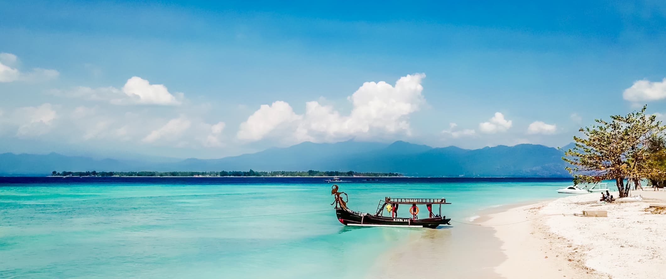 a gorgeous beach with a boat parked along the shore in the Gili Islands, Indonesia