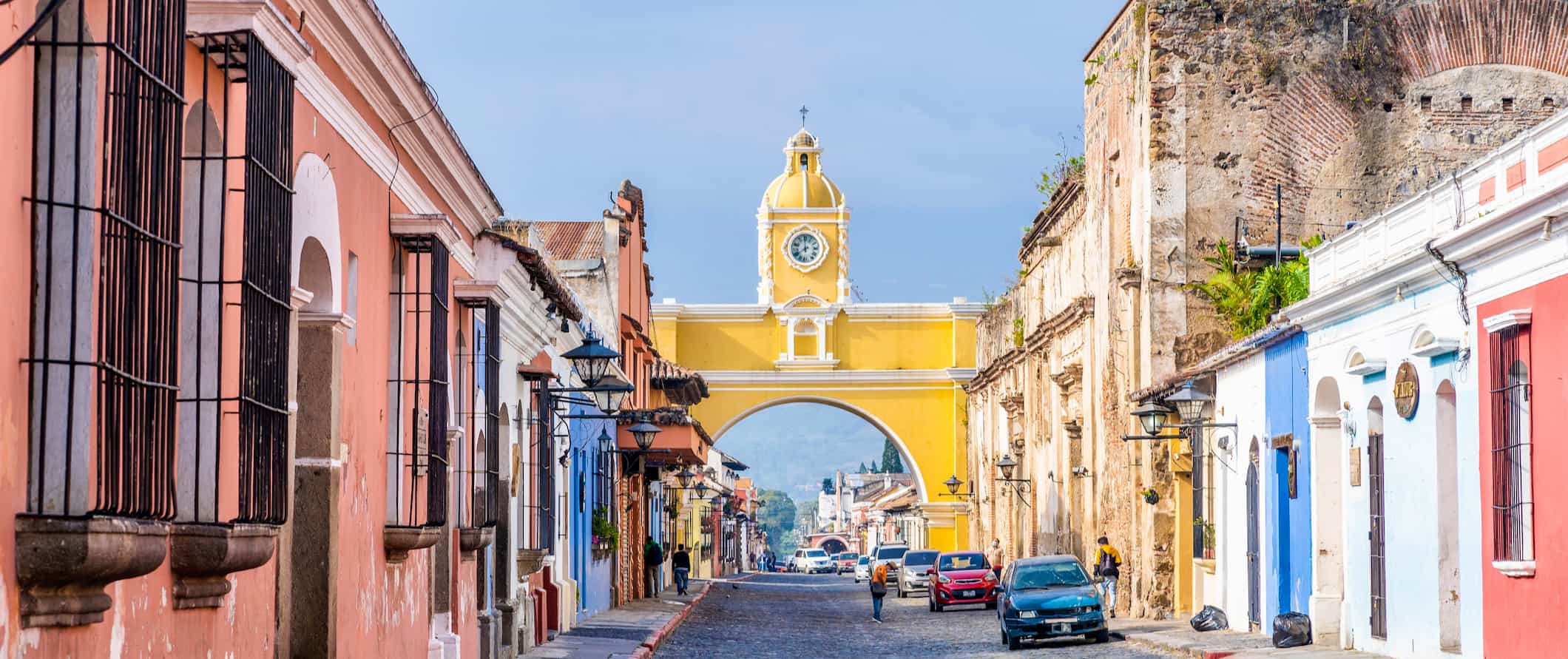 Cobblestone-lined street with brightly colored low buildings on both sides, with a yellow archway going over the street in Guatemala
