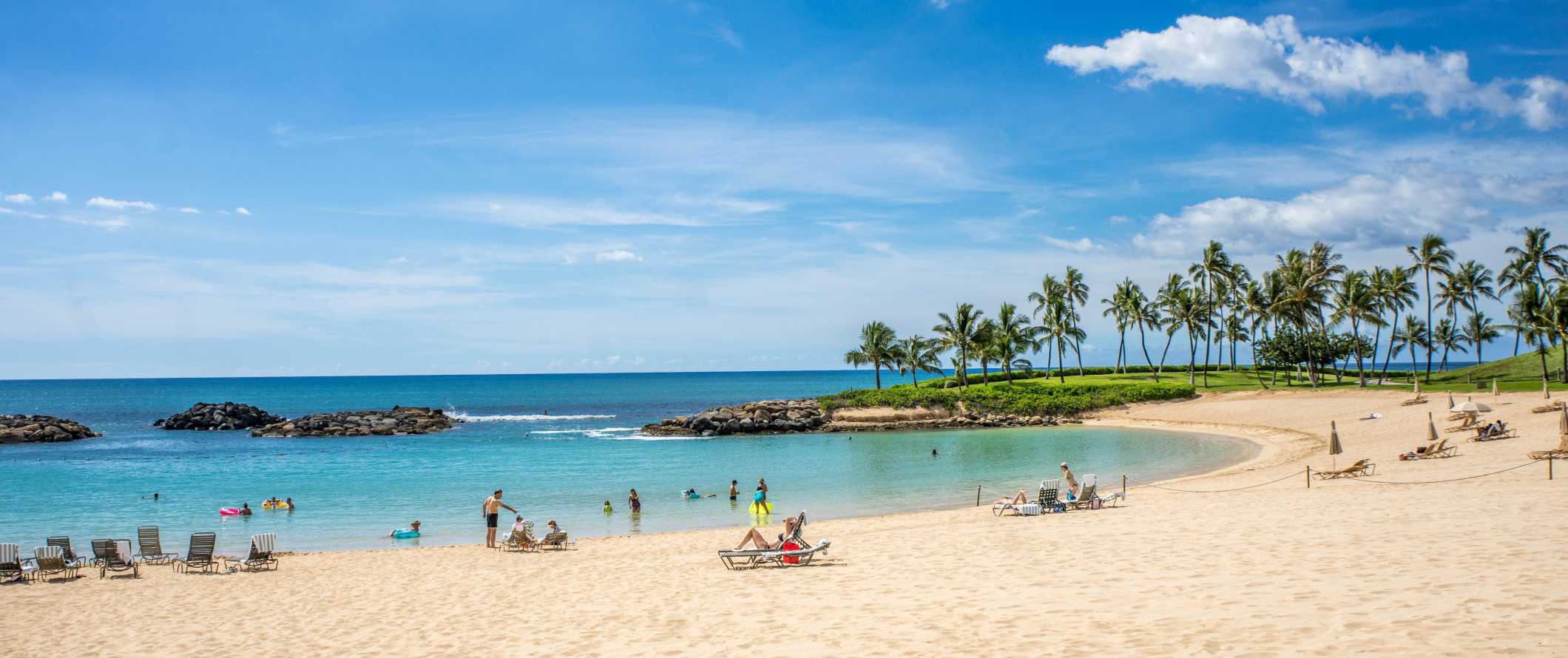 People lounging on the beach with palm trees in the background in Hawaii.