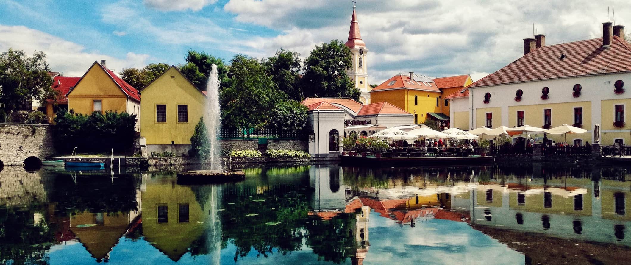 a colorful and historic town in Hungary, with a reflection over the calm waters