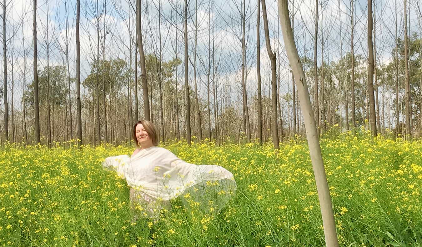 In India, a single woman stands in a green field surrounded by grass and trees.