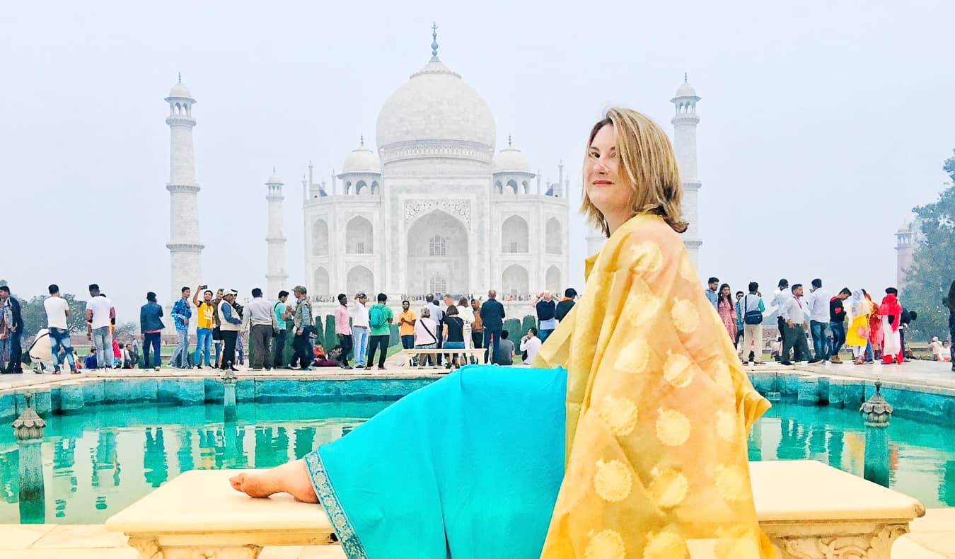 A lone female traveler wearing a bright sari stands in front of the Taj Mahal in India.