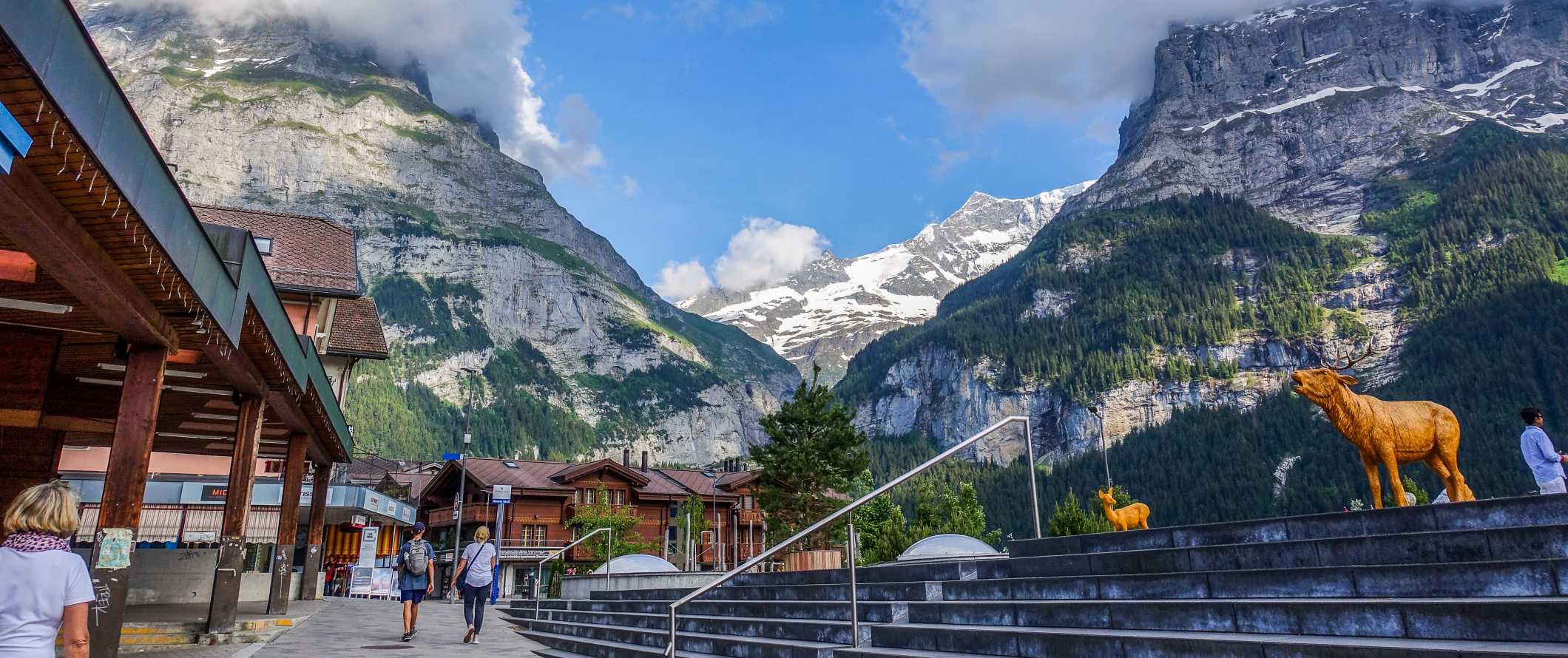 People walking around a street amongst wooden chalets with dramatic mountains rising up in the background in Interlaken, Switzerland
