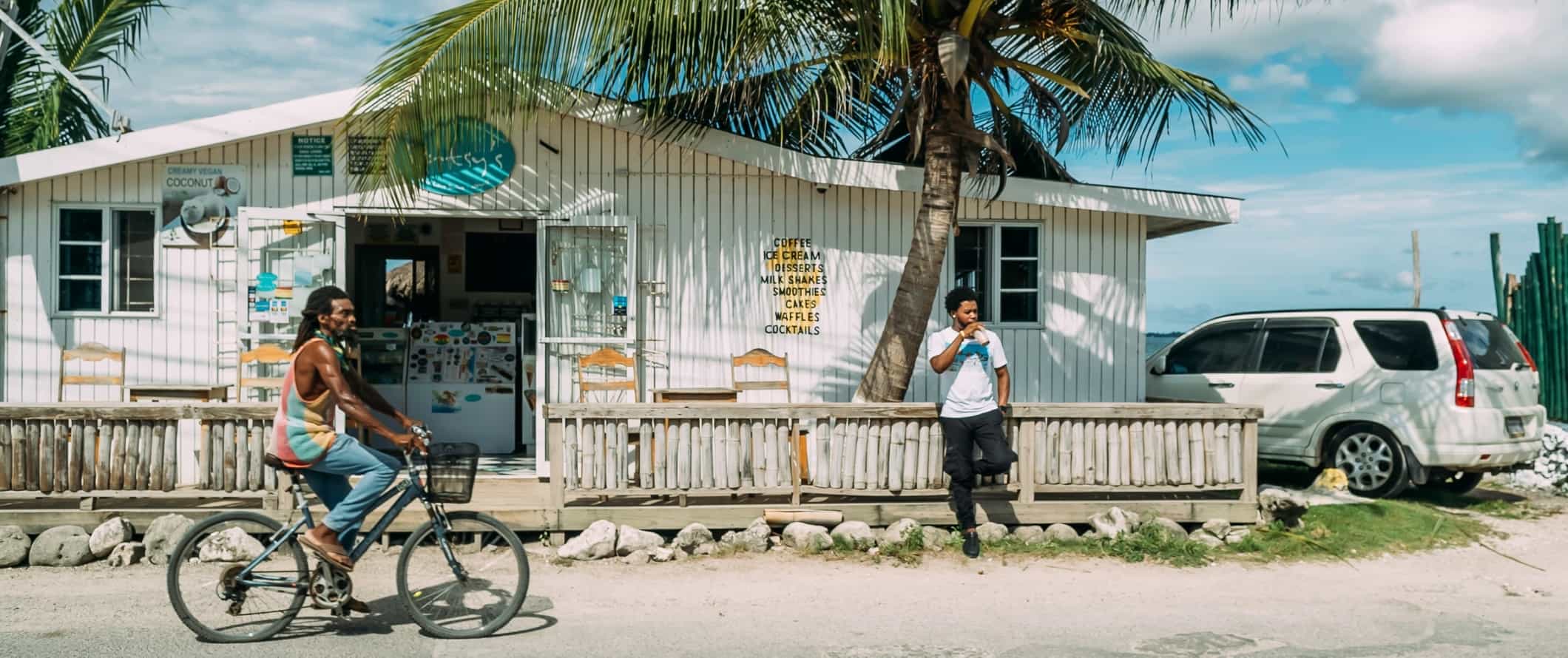 Man biking down the street in front of a white bungalow in Jamaica