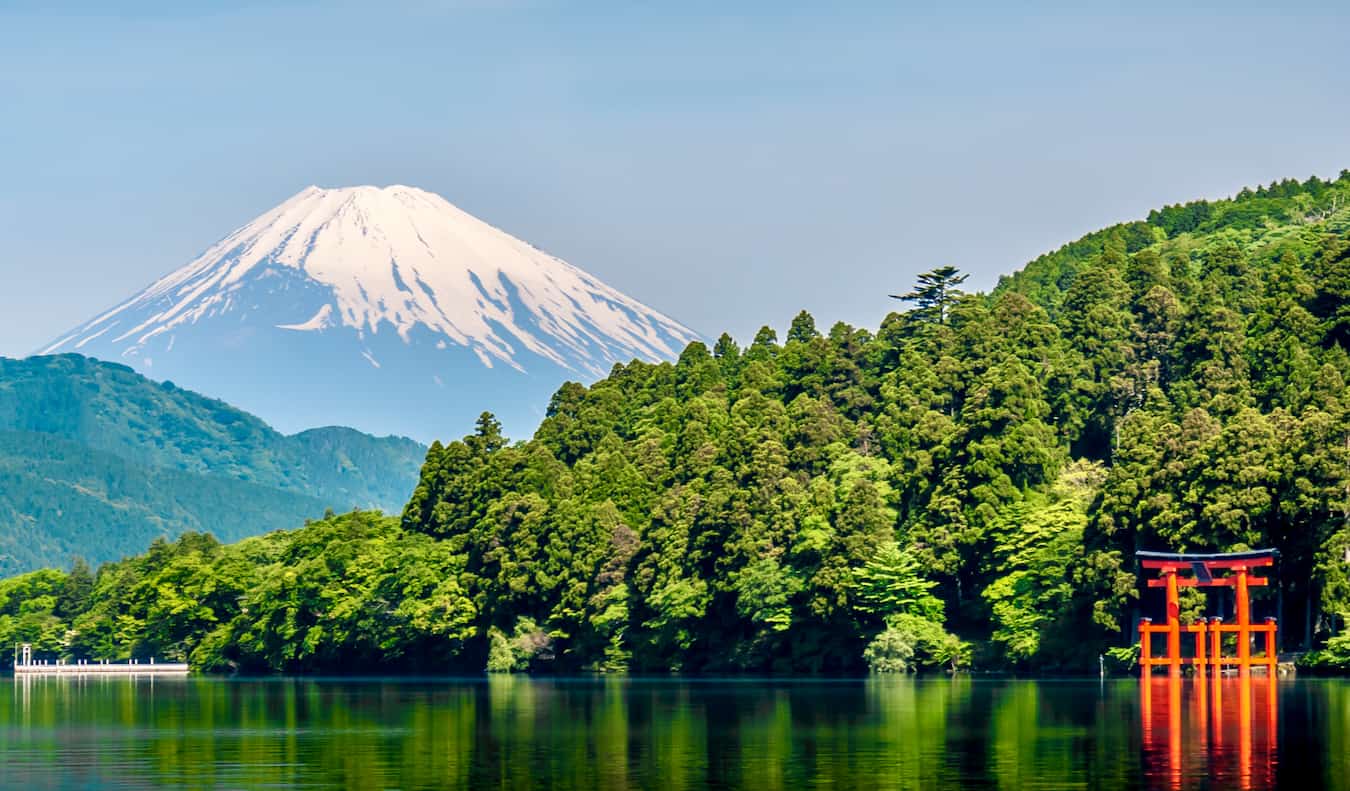 A red torii gate in the water with lush greenery and Mount Fuji in the background Japan