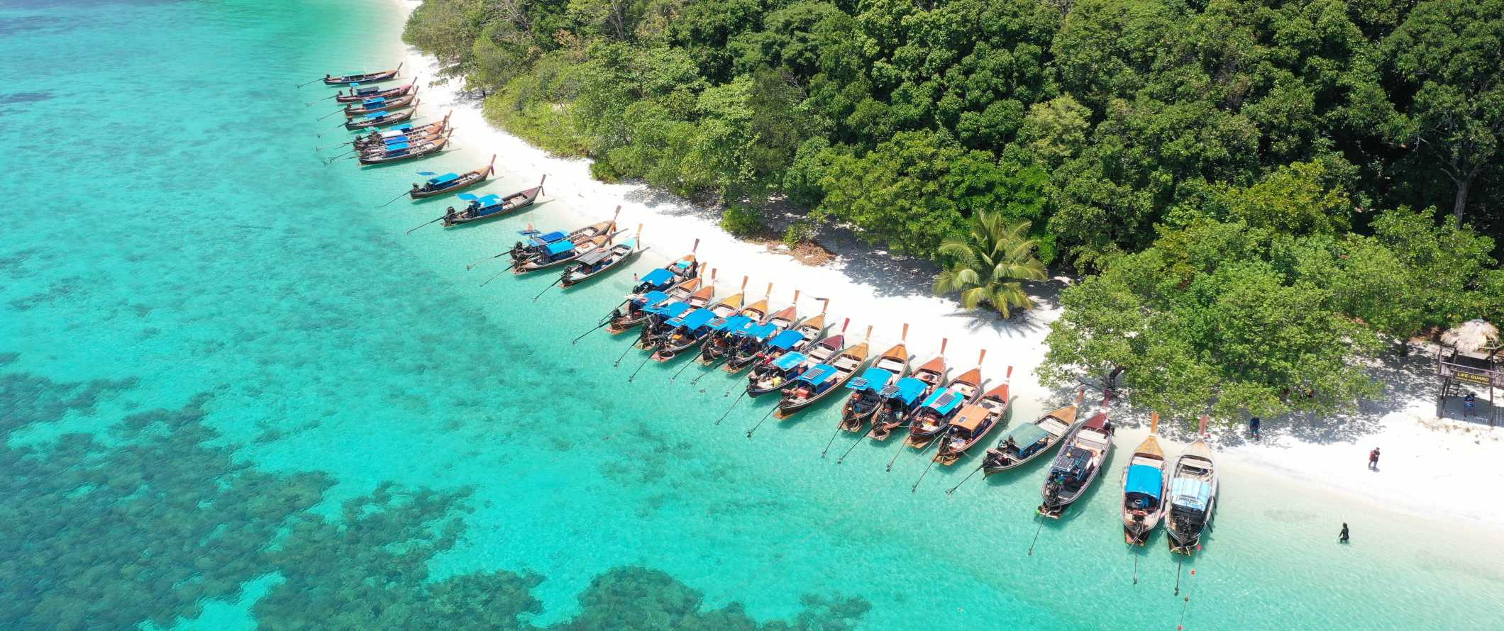 Aerial view of a line of longtail boats docked on a beach on the island of Ko Lipe, Thailand