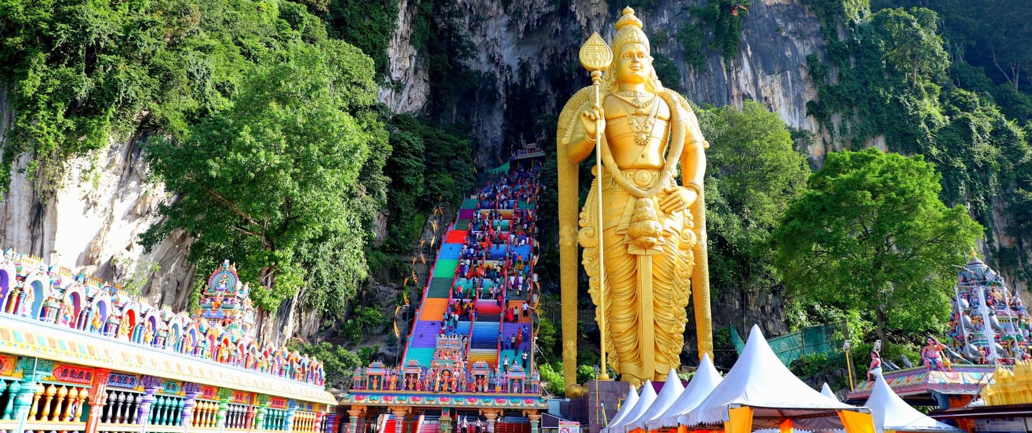 The entrance to the Batu caves with colorful steps and a huge golden statue of Arulmigu Murugan, a Hindu deity in Malaysia