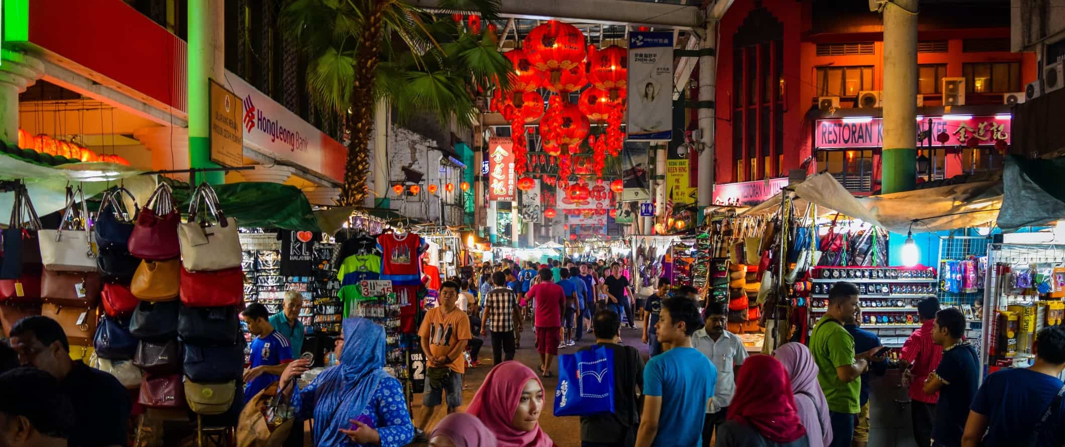 People walking down a crowded pedestrianized street lined with shops at night in Kuala Lumpur, Malaysia
