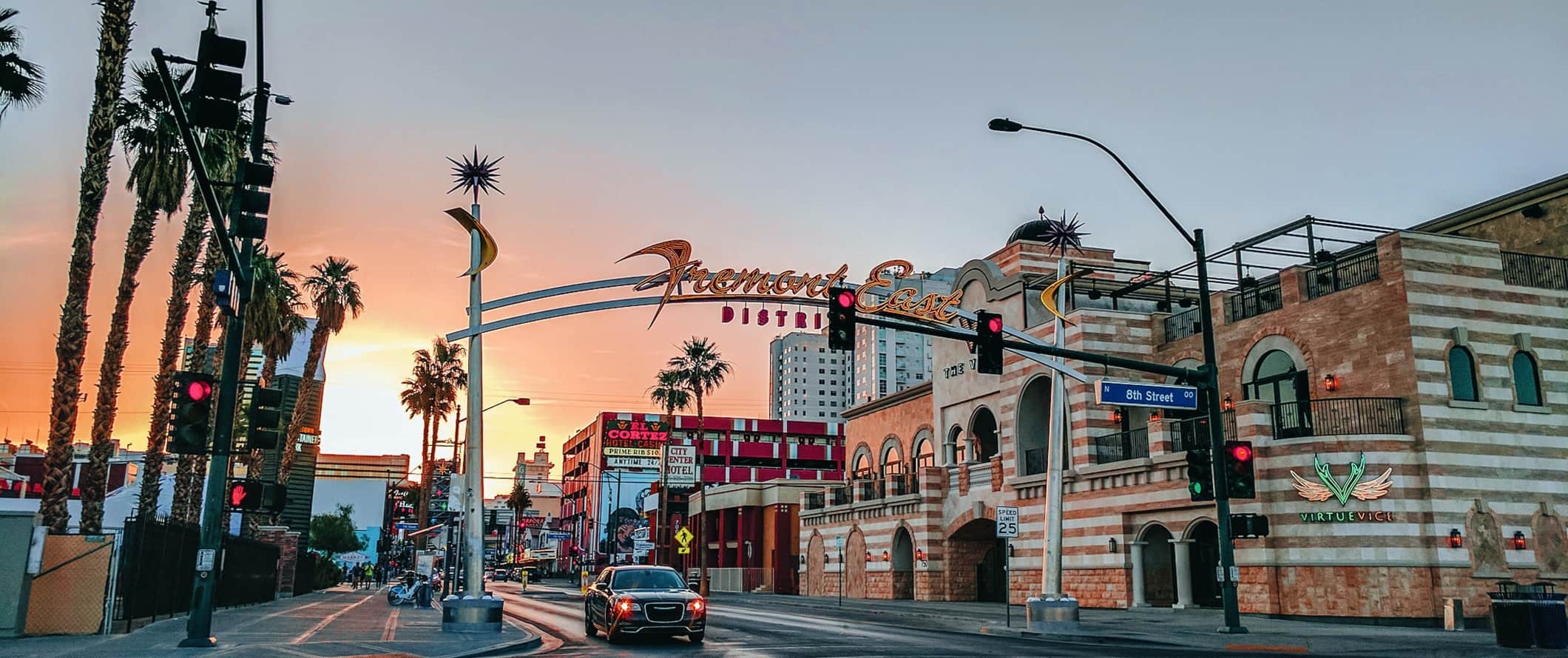 Neon sign stretching over a palm-tree-lined street at sunset, saying 