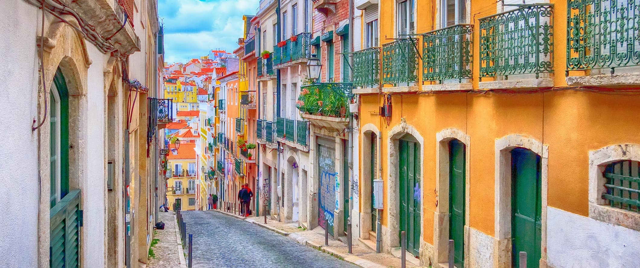Locals walking down a narrow, colorful street in Lisbon, Portugal