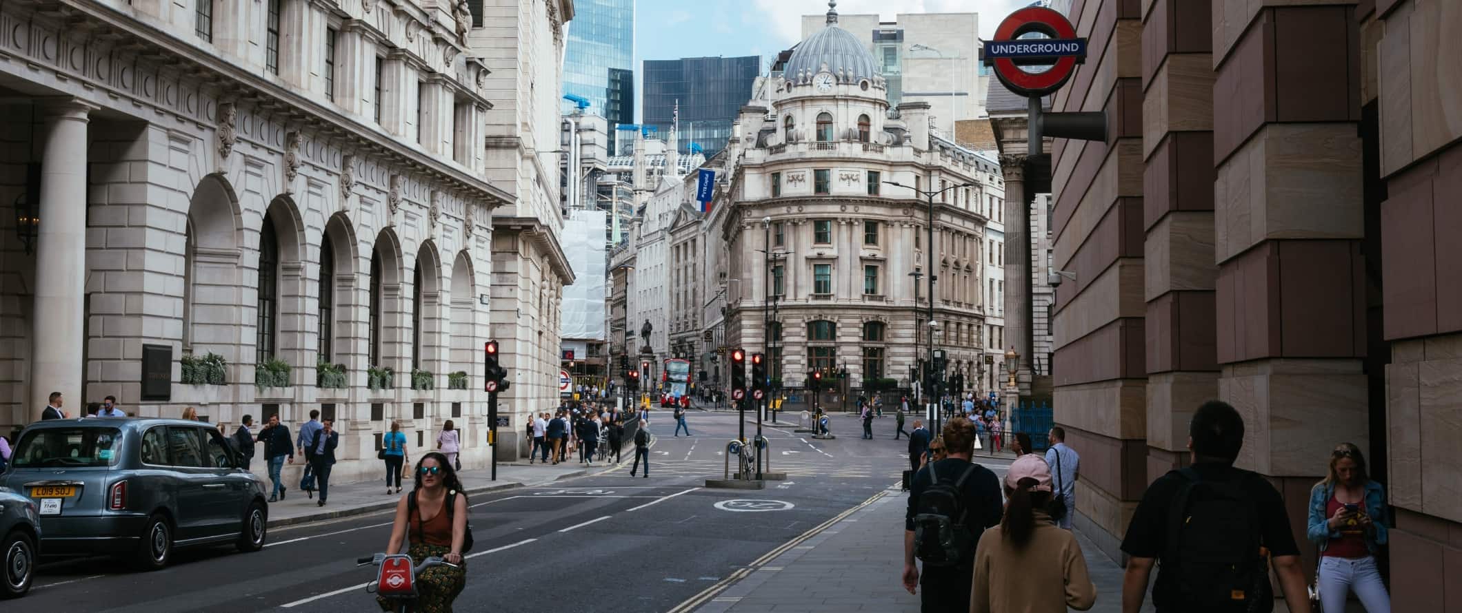 Street scene with people walking around under a sign for the Underground in London, England