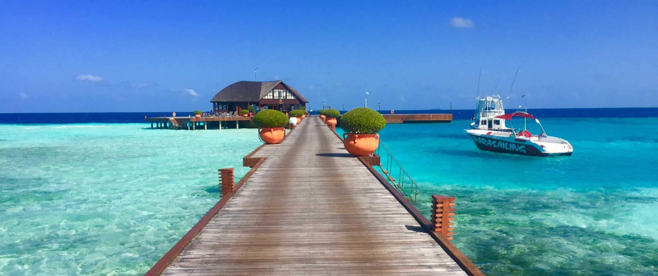 Boats anchored by a dock with a large over-water bungalow in the Maldives